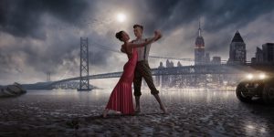 A cross processed image of a vintage retro styled romantic hetrosexual couple dancing in bare feet on a beach a low tide. The dancers are lit by the headlights on a vintage car and are dancing on a deserted beach close to a suspension bridge and city skyscrapers in the background.